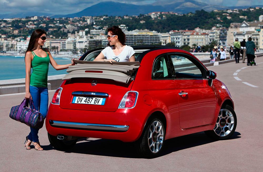 Fiat 500 descapotable con una chica asomando por el techo y otra chica parada mirándola